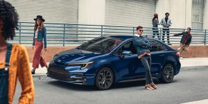 A blue Toyota sedan parked on an urban street and surrounded by fashionable drivers.