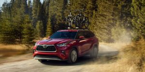 A red Toyota Highlander driving on a dirt road through a forest, with bicycles mounted on the roof.