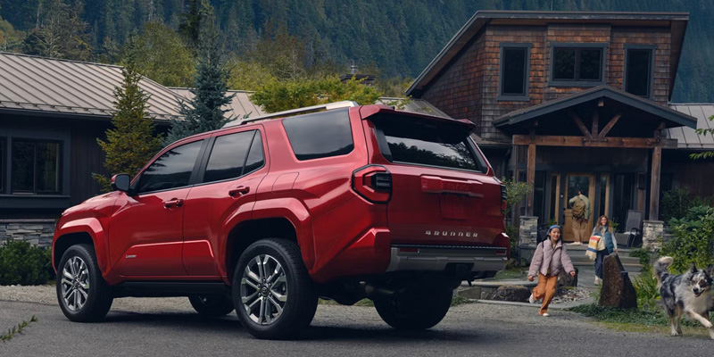 Red Toyota 4Runner SUV parked near a mountain cabin surrounded by nature.
