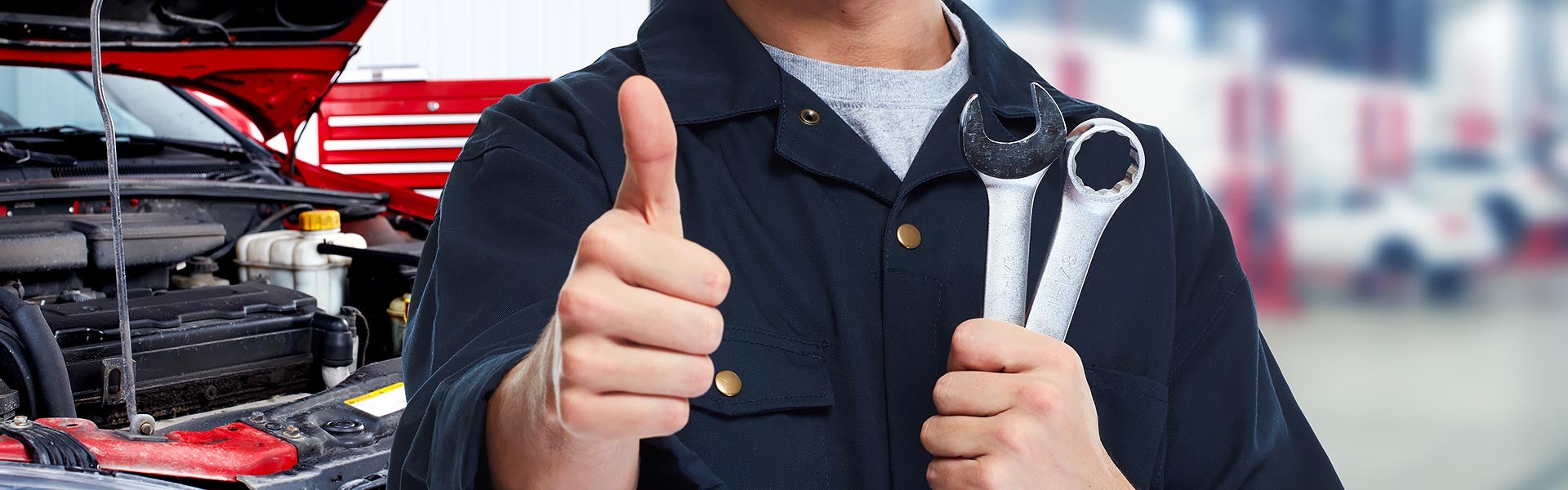 Mechanic holding wrenches beside an open vehicle engine.